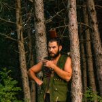 man wearing a khaki top waiting by the tree
