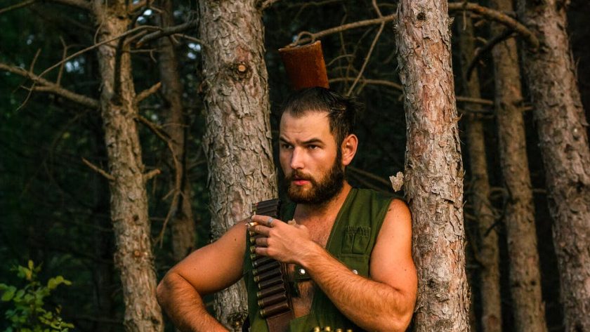 man wearing a khaki top waiting by the tree